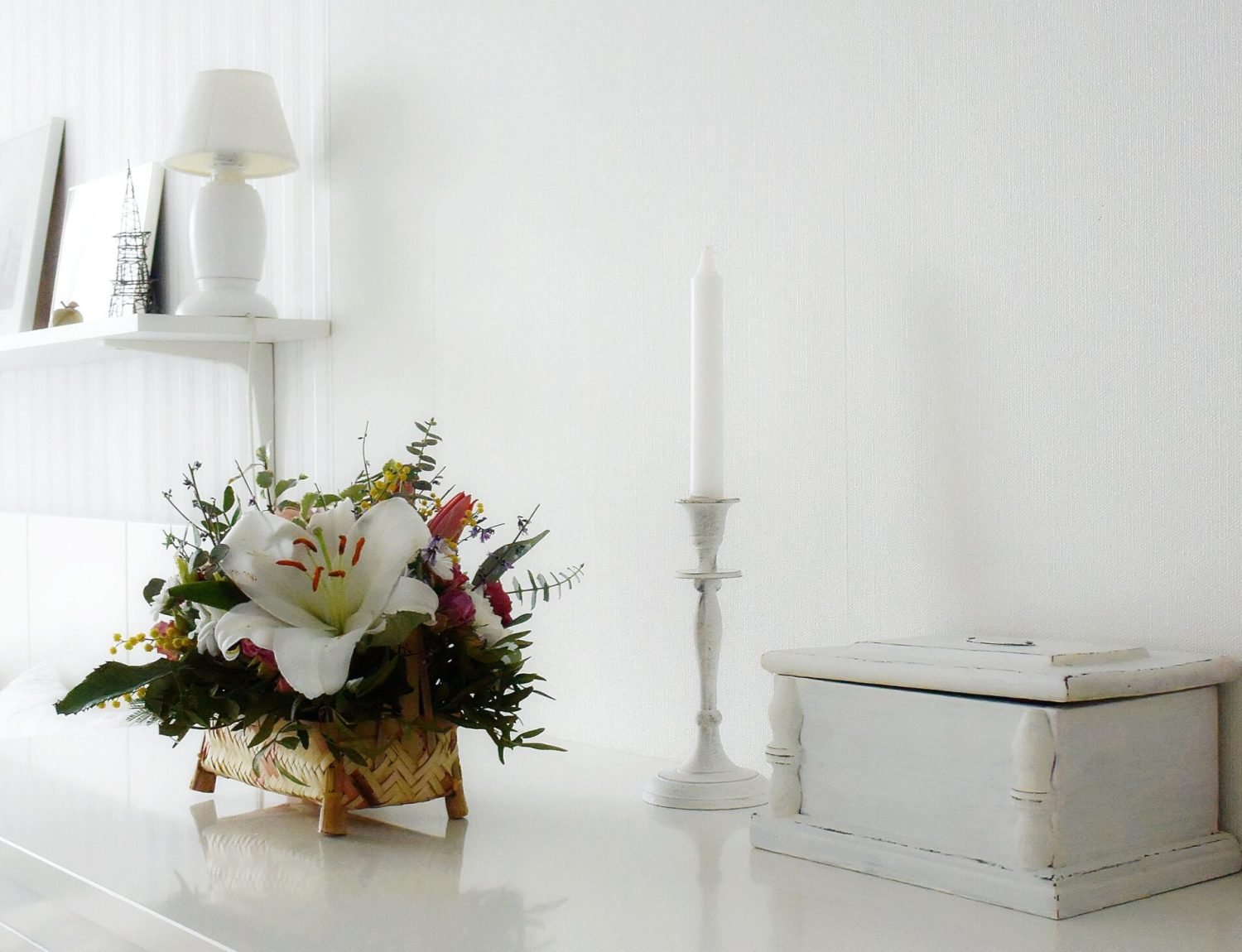 Elegant minimalist white interior with a flower arrangement and candle on a table.